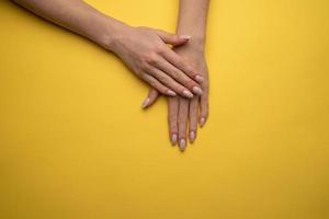 mãos femininas com uma bela manicure em um fundo amarelo, vista superior foto