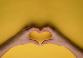 coração fazendo as mãos da mulher com manicure em fundo amarelo, vista superior foto