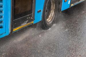 ônibus municipal azul movendo-se na estrada chuvosa com salpicos de água foto