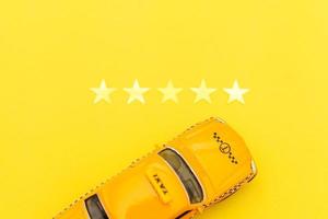 táxi de carro de brinquedo amarelo e classificação de 5 estrelas isolada em fundo amarelo. aplicativo para smartphone do serviço de táxi para pesquisa on-line chamando e reservando o conceito de táxi. símbolo de táxi. copie o espaço. foto