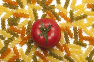 macarrão, colorido, cru, com tomate em uma mesa branca. foto