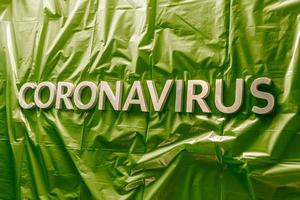 palavra coronavírus colocada com letras prateadas em casaco de plástico verde amassado - em perspectiva com foco seletivo foto