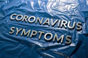 as palavras sintomas de coronavírus colocadas com letras prateadas em filme plástico azul amassado - composição de perspectiva diagonal foto