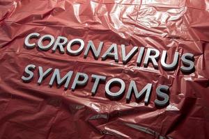 as palavras sintomas de coronavírus colocadas com letras prateadas em filme plástico vermelho amassado - composição de perspectiva diagonal foto