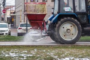 tula, rússia - 21 de novembro de 2020, trator espalhando reagente de sal no pavimento da cidade à luz do dia de inverno. foto