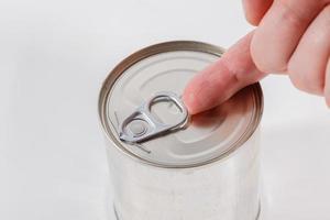mão caucasiana nua abre uma lata com um anel de tração em um fundo branco foto