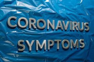 as palavras sintomas de coronavírus colocadas com letras prateadas em filme plástico azul amassado - composição de perspectiva linear com foco seletivo foto
