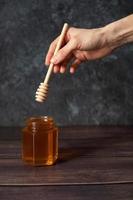 a mão segura um palito de mel. um pote de mel. fundo escuro. foto