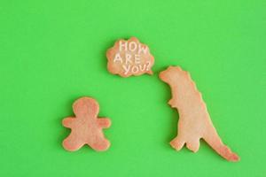 biscoitos caseiros em formas de dinossauro e homem com inscrição - como você está - sobre fundo verde, vista superior. biscoito doce com esmalte branco. foto