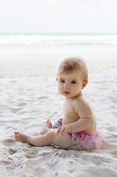 sincero retrato de adorável menina na areia na praia no fundo do mar. desenvolvimento sensorial para crianças ao ar livre. foto