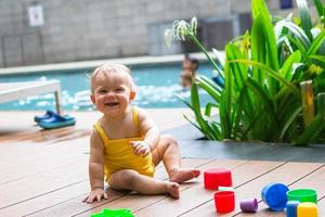 menina sorridente com joelhos sujos brincando ao ar livre com construtor de plástico colorido em um fundo de plantas verdes e piscina. foto