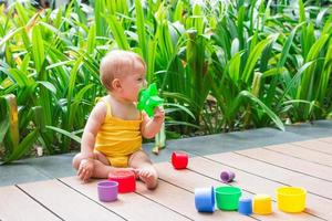 sorridente menina brincando ao ar livre com construtor de plástico colorido em um fundo de plantas verdes. foto