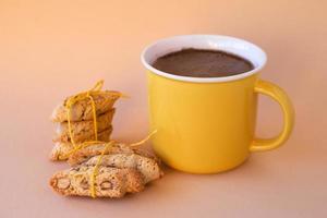 xícara amarela com café preto e biscoitos de amêndoa cantuccini com fita amarela sobre fundo rosa. foto