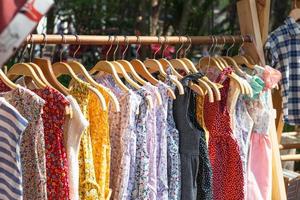 cabides de madeira com cabides e com vestidos coloridos. vitrine com roupas no mercado de rua. foto