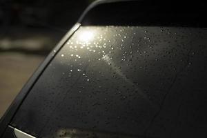 janela traseira do carro preto. gotas na janela traseira do transporte. luz na janela do carro. foto