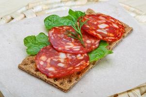 sanduíche de salame na placa de madeira e fundo de madeira foto