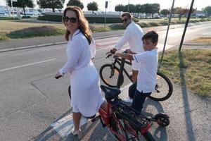 família feliz desfrutando de uma bela manhã à beira-mar juntos, pais andando de bicicleta e seu filho andando de scooter elétrico. foco seletivo foto