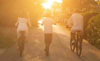 família feliz desfrutando de uma bela manhã juntos, pais andando de bicicleta e seu filho andando de scooter elétrico. foco seletivo foto