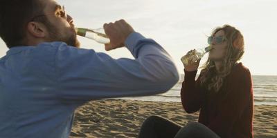 amoroso jovem casal sentado na praia ao lado da fogueira bebendo cerveja foto