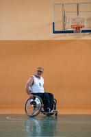 um inválido de guerra em uma cadeira de rodas treina com uma bola em um clube de basquete em treinamento com equipamentos esportivos profissionais para deficientes. o conceito de esporte para pessoas com deficiência foto