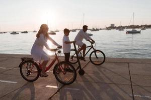 família feliz desfrutando de uma bela manhã à beira-mar juntos, pais andando de bicicleta e seu filho andando de scooter elétrico. foco seletivo foto