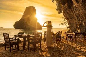 turista de mulher em jantar de vestido branco na caverna do restaurante na praia de phra nang ao pôr do sol, railay, krabi, tailândia. férias, viagens, verão, desejo de viajar e conceito de férias