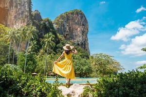 turista de mulher de vestido amarelo e chapéu viajando na praia de railay, krabi, tailândia. férias, viagens, verão, desejo de viajar e conceito de férias foto