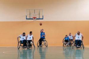 veteranos de guerra deficientes em cadeiras de rodas com equipamento profissional jogam basquete no salão. o conceito de esportes com deficiência foto