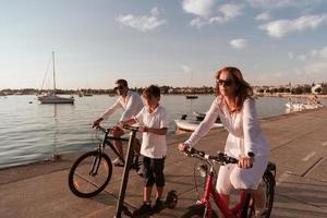 família feliz desfrutando de uma bela manhã à beira-mar juntos, pais andando de bicicleta e seu filho andando de scooter elétrico. foco seletivo foto