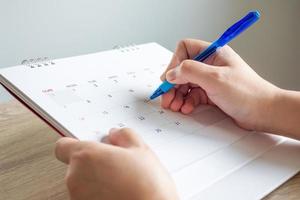 mão de mulher com caneta escrevendo na data do calendário conceito de reunião de planejamento de negócios foto