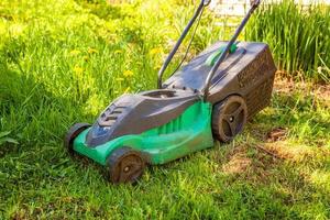 cortador de grama cortando grama verde no quintal em dia ensolarado. fundo de estilo de vida do país de jardinagem. bela vista no gramado de grama verde fresca à luz do sol, paisagem de jardim na primavera ou verão. foto