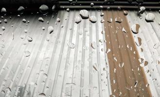 gotas de chuva na frente do vidro no pano de fundo do telhado prateado foto