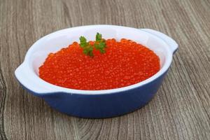 caviar vermelho em uma tigela sobre fundo de madeira foto