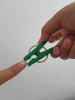 uma mão tenta beliscar o polegar usando um prendedor de roupa verde. foto