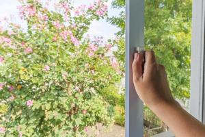 mão segure a alça da tela de arame da rede mosquiteira na janela da casa foto