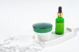 conjunto de cosméticos sem marca para rotina de cuidados com a pele. frasco de creme facial e frasco conta-gotas de vidro com óleo essencial ou soro de beleza na bandeja de concreto no fundo branco foto