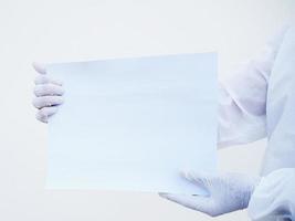 closeup mãos de médico ou cientista em uniforme de conjunto de ppe segurando papel em branco para texto com as duas mãos enquanto olha para a frente. coronavírus ou covid-19 conceito isolado fundo branco foto