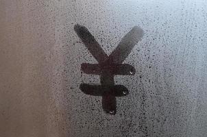 símbolo do iene chinês é escrito com um dedo na superfície do vidro embaçado foto