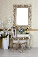 um fragmento de um interior retrô com uma cadeira e uma mesa, na qual há um telefone e um vaso de flores. acima da mesa está pendurado um porta-retrato vazio para sua foto