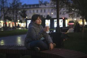 um adolescente com emoções positivas e um copo de papel na mão na rua em uma noite escura de outono no contexto das luzes da cidade. foto