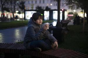 um adolescente solitário com emoções pensativas e um copo de papel na mão na rua em uma noite escura de outono no contexto das luzes da cidade. foto