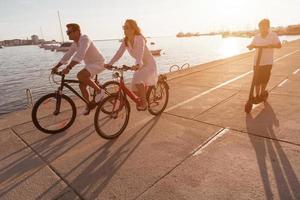 família feliz desfrutando de uma bela manhã à beira-mar juntos, pais andando de bicicleta e seu filho andando de scooter elétrico. foco seletivo foto