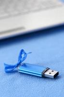 cartão de memória flash usb azul brilhante com um laço azul repousa sobre um cobertor de tecido de lã azul claro macio e peludo ao lado de um laptop branco. design de presente feminino clássico para um cartão de memória foto