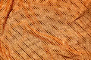 fundo de textura de tecido de vestuário esporte laranja. vista superior da superfície têxtil de pano laranja. camisa de basquete brilhante. espaço de texto foto