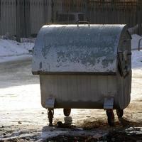 um recipiente de lixo prateado fica perto de edifícios residenciais no inverno foto