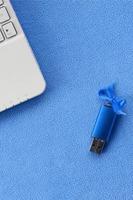 cartão de memória flash usb azul brilhante com um laço azul repousa sobre um cobertor de tecido de lã azul claro macio e peludo ao lado de um laptop branco. design de presente feminino clássico para um cartão de memória foto