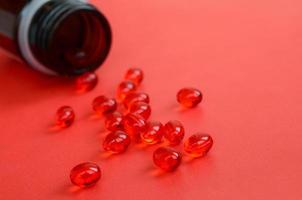 muitos comprimidos vermelhos transparentes foram espalhados de um pequeno frasco de vidro marrom em uma superfície vermelha foto