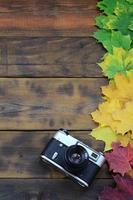 a câmera antiga entre um conjunto de folhas de outono caídas amareladas em uma superfície de fundo de tábuas de madeira naturais de cor marrom escura foto