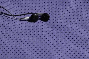 fones de ouvido pretos repousam sobre a roupa esportiva violeta de fibra de nylon de poliéster. o conceito de ouvir música durante o treinamento esportivo com tecnologia moderna foto