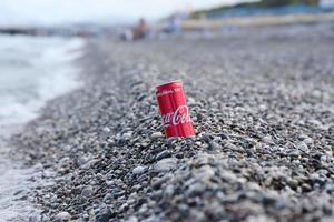 antalya, turquia - 18 de maio de 2021 lata vermelha original da coca cola encontra-se em pequenas pedras redondas perto da costa do mar. coca-cola na praia turca foto